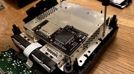 Clockwise, from top left: 1) What you'll need for the mod. 2) Remove the lid and you'll find that there are lots of screws to remove in order to detach the GameCube's optical drive assembly. 3) Under the drive, you'll need to remove more screws to detach the actual optical drive – the GC Loader connects to the metal plate, which you'll need to retain. 4) The GC Loader slots into the connection which was used to link the drive to the mainboard.